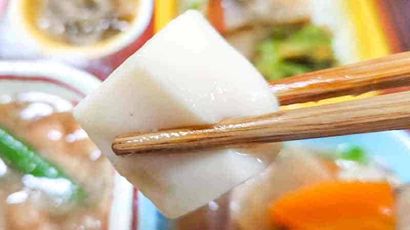 低糖質セレクトBの鶏肉の時雨煮と鮭の塩焼きの副菜のけんちん煮の具材の豆腐を箸で持ち上げた時の写真です。