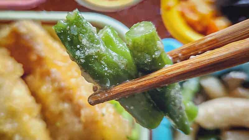 鰈の唐揚げと野菜の旨煮の副菜いんげんひらたけ胡麻和えのいんげんを箸で持ち上げた写真です