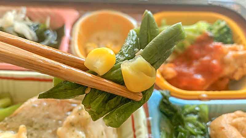 食宅便の低糖質セレクトE赤魚のソテーバター風味の副菜いんげんとコーンの胡麻和えを箸で持ち上げている写真